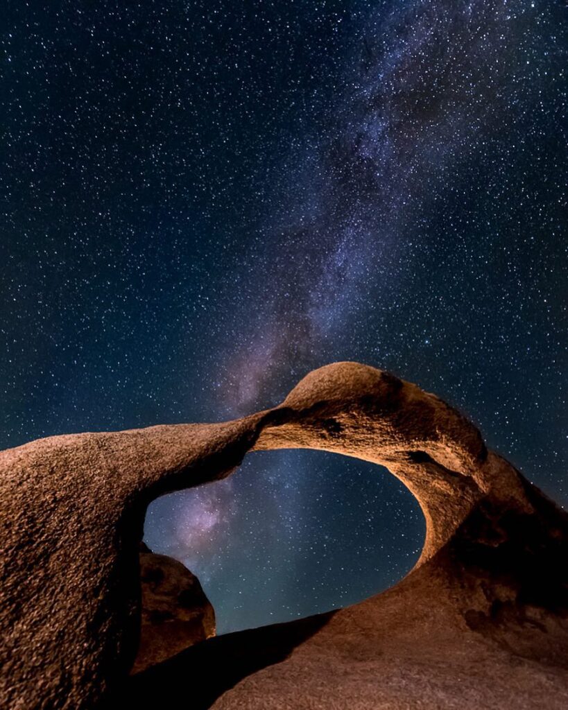 A starry night sky with the Milky Way visible through a natural rock arch formation in Bishop, California, nestled in the Eastern Sierra. visit bishop