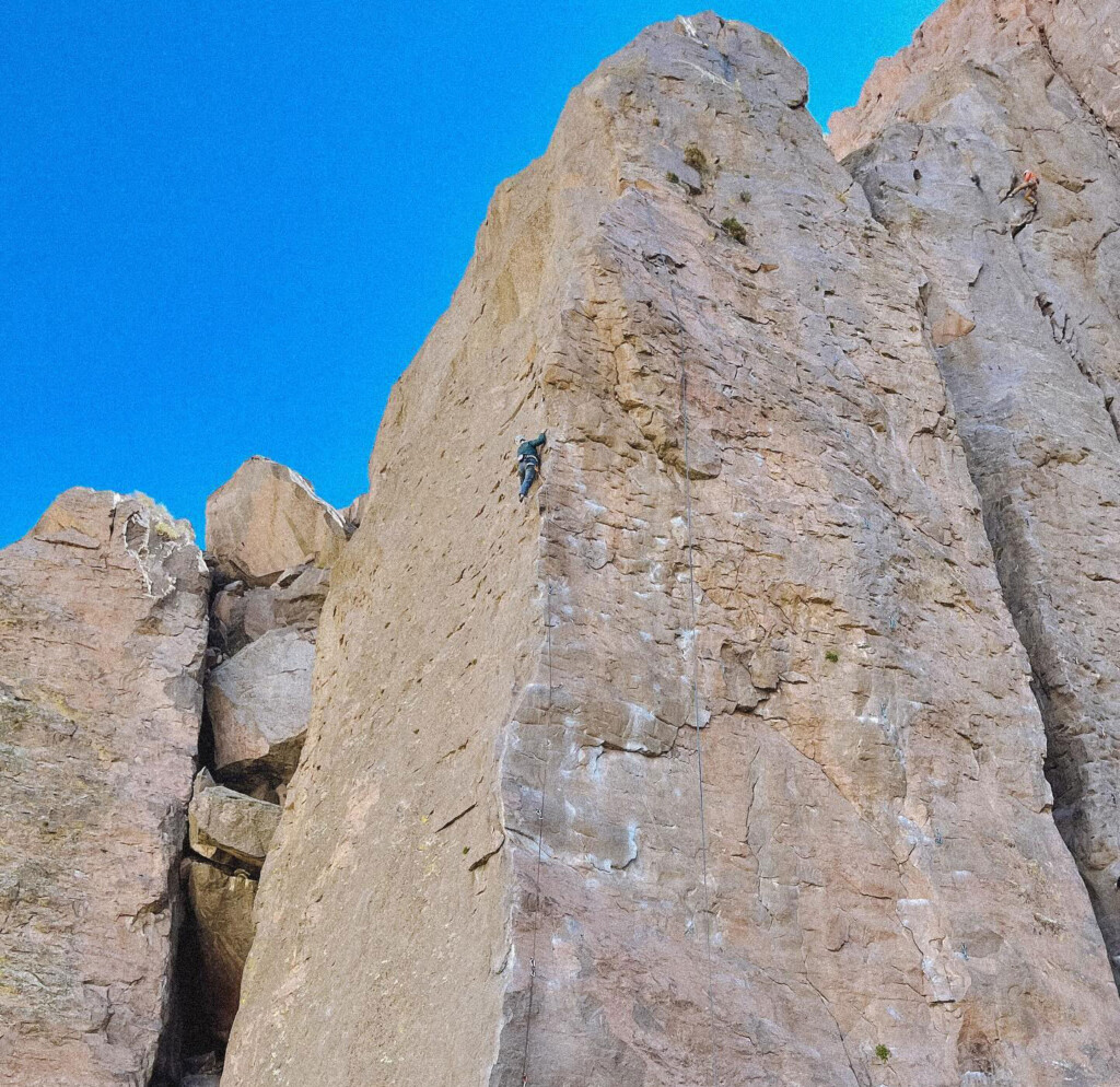 Two rock climbers ascend a steep, rocky cliff against a clear blue sky backdrop in the majestic Eastern Sierra near Bishop, California. visit bishop