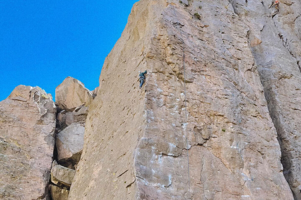 Two rock climbers ascend a steep, rocky cliff against a clear blue sky backdrop in the majestic Eastern Sierra near Bishop, California. visit bishop