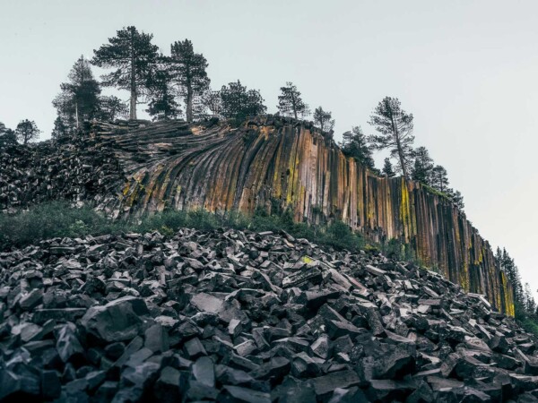 Rock formation with vertical basalt columns, mostly fallen, surrounded by pine trees and boulders under a cloudy sky in the breathtaking Eastern Sierra near Bishop, California. visit bishop