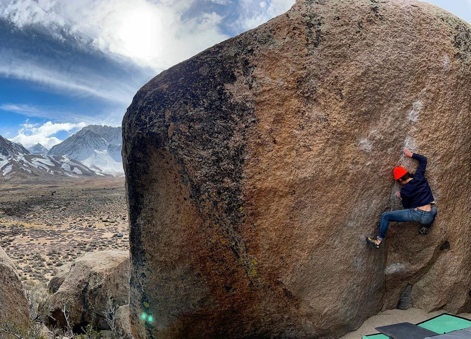 Person bouldering on a large rock with a mountainous landscape and cloudy sky in the background, set in the stunning terrain of Bishop, California in the Eastern Sierra. visit bishop