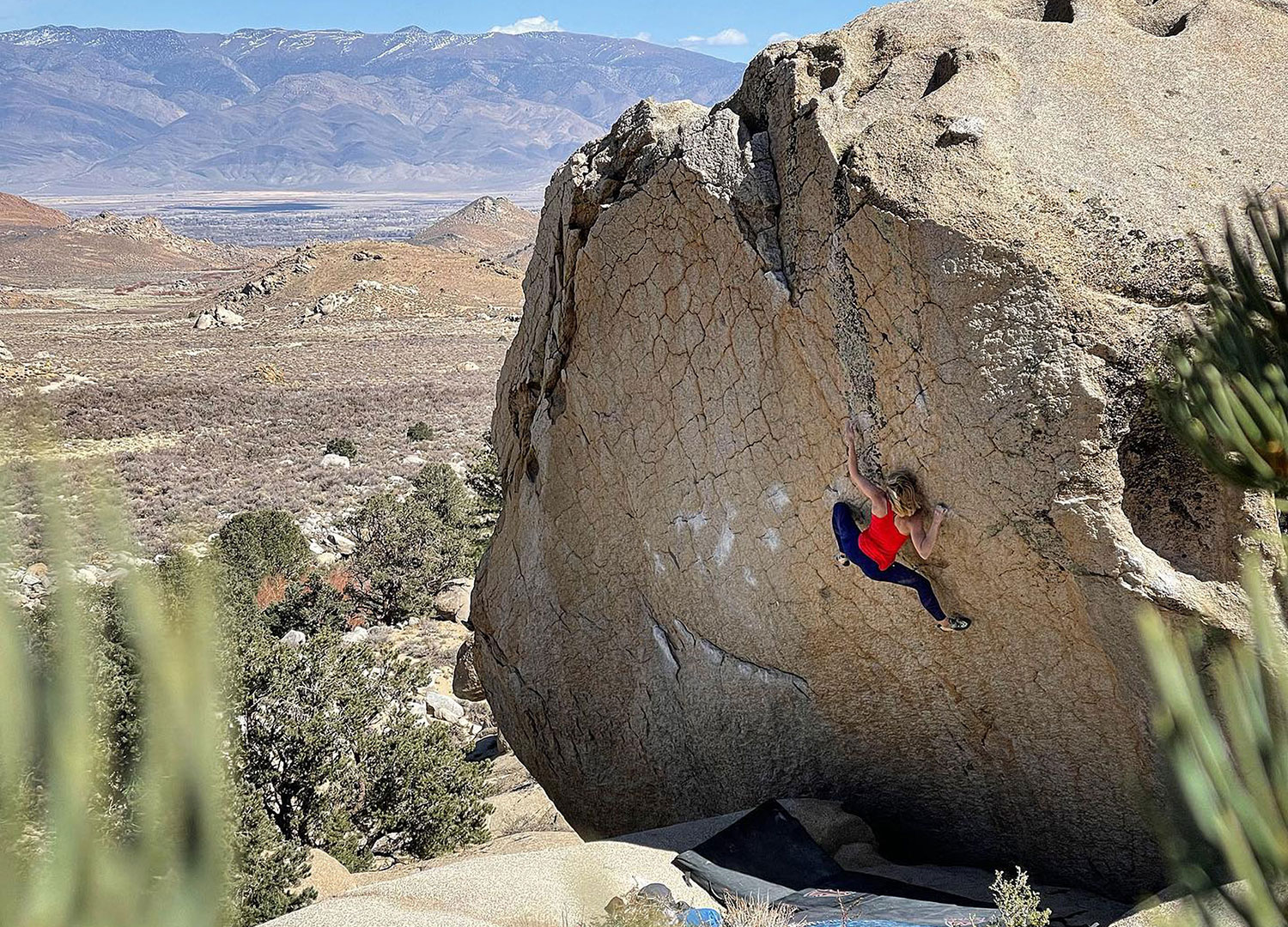 Person in a red shirt climbing a large rock face in the Eastern Sierra near Bishop, California, on a clear day. visit bishop