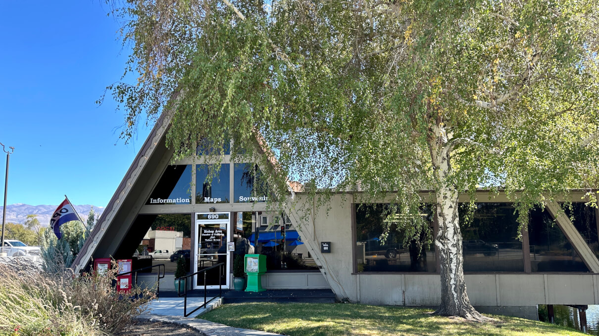 A triangular building with large windows, trees in front, and a "Visitor Center" sign near the entrance, welcomes you to the heart of Bishop, California. visit bishop