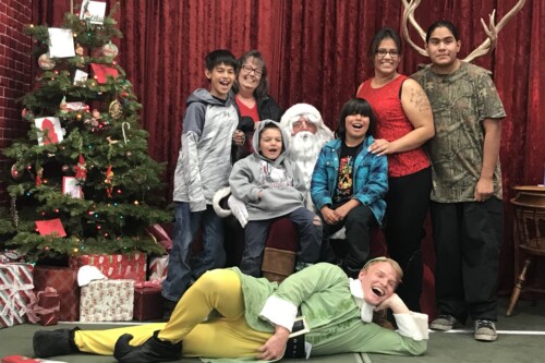 A family poses with Santa Claus and an elf in front of a decorated Christmas tree and a velvet curtain backdrop, capturing the holiday spirit in Bishop, California. visit bishop
