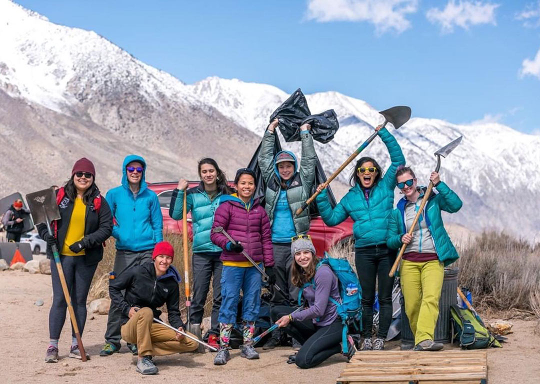 A group of people in winter clothing, smiling and holding shovels and tools, stands proudly in the snowy landscape of the Eastern Sierra near Bishop, California. visit bishop