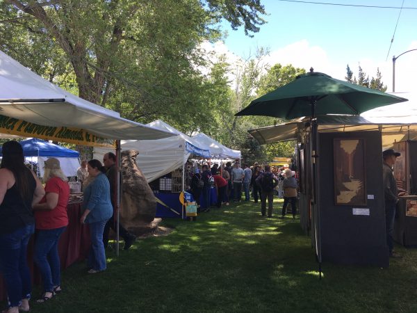 People browsing stalls at an outdoor market with trees providing shade. visit bishop