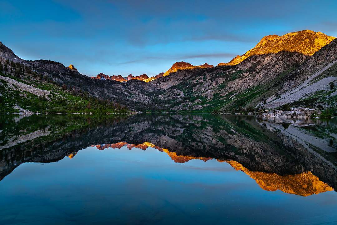 Reflection of mountains on glass-like lake with sun shining on peaks at sunrise. Lake Sabrina. Bishop Visitor