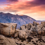 Climber on huge boulder with mountain in background at sunset