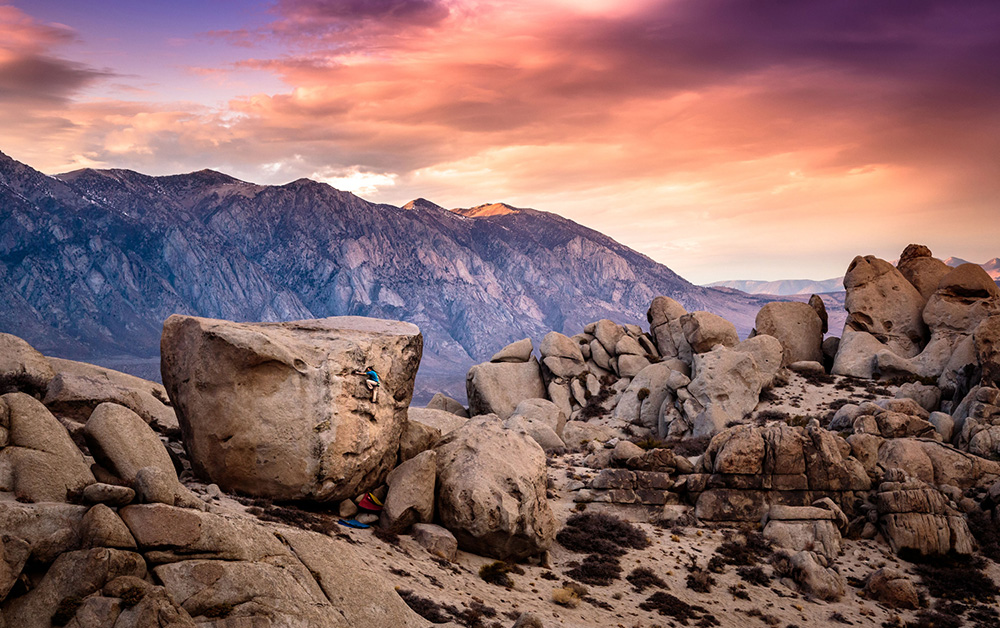 Climber on huge boulder with mountain in background at sunset