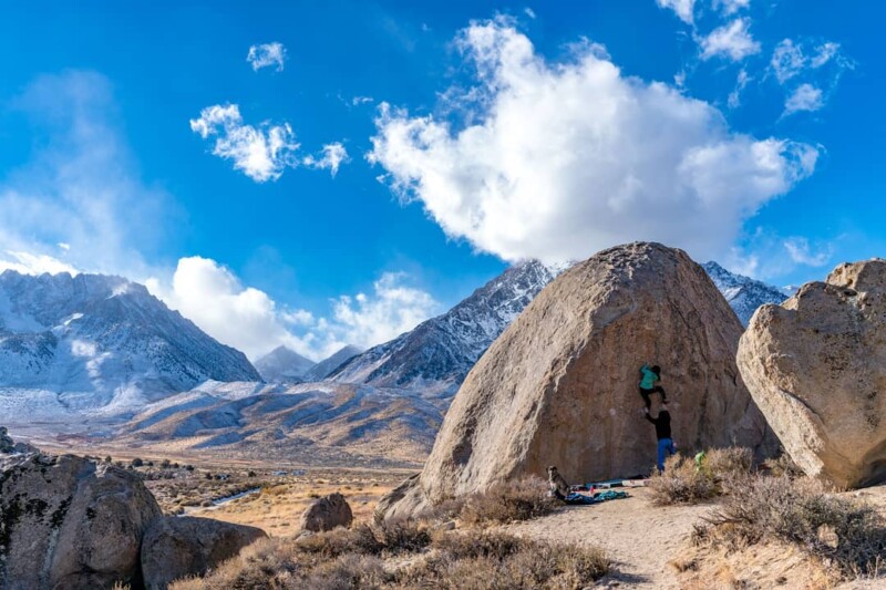 Climber on large boulder with snow covered mountains in background.