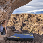 Climber sits at the base of an overhanging boulder.