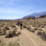 Mountain bikers on dirt trail with mountains in background. v